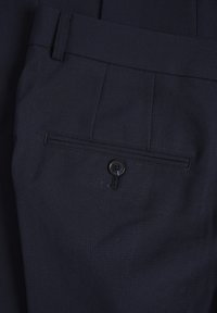 Marinblå byxor med texturerat tyg, veckad design och en bakficka med en svart knappdetalj.