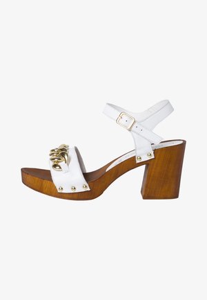 Sandale plateforme en cuir blanc avec quincaillerie dorée, talon en bois épais et clous décoratifs sur la bride supérieure. Bride de cheville ajustable.