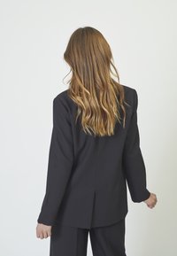 Black tailored blazer with a structured fit, long sleeves, and a single vent at the back. Smooth fabric with a matte finish.
