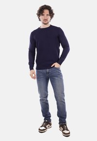 Maglione a maglia blu navy con motivo testurizzato, scollo rotondo e maniche lunghe. Indossato con jeans azzurri e sneakers marroni.