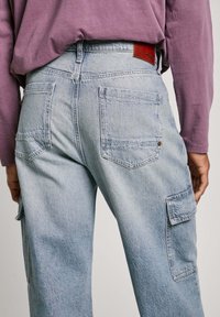Pantalones cargo de mezclilla azul claro con un corte relajado, que cuentan con múltiples bolsillos y una etiqueta de cuero en la parte trasera de la cinturilla. Acabado texturizado.