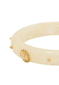 Bracelet en ivoire translucide avec effet marbré, mettant en avant un accent en forme de soleil doré et de petites rivets dorés. Texture lisse et forme ronde.