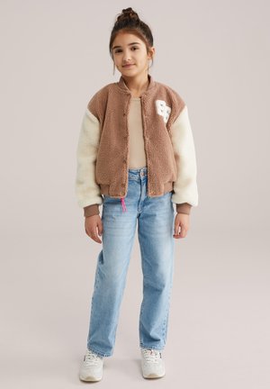 Hnedo-krémová bomber bunda s plyšovou textúrou, rebrovanými manžetami a predným nášivkovým detailom. Svojím vzhľadom doplnená svetlými džínsami a bielymi teniskami.