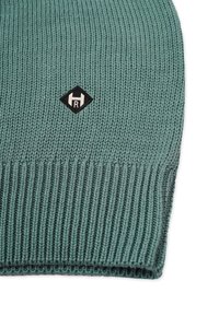 Knit beanie in a muted green color, featuring a ribbed texture and a small black diamond logo with white lettering on the front.