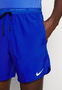 Pantalones cortos de running Nike en azul brillante, con un cordón negro, tejido transpirable y un logo blanco en el dobladillo. Diseño sencillo con bolsillos.