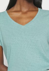 Světle modré tričko s výstřihem do V vyrobené z jemné, texturované tkaniny, s volným střihem a krátkými rukávy, které má decentní melírovaný vzor.