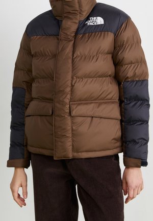 Veste matelassée marron et noire avec deux poches avant à rabat, portée par une personne avec un pantalon en velours côtelé marron.