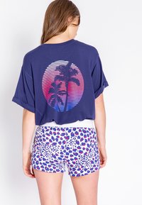 Marineblauwe oversized t-shirt met een gedetailleerde zonsondergangafbeelding en palmbomen. Gecombineerd met witte shorts, versierd met een kleurrijk dierenprintpatroon.