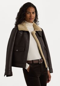 Veste en cuir marron avec un col en shearling beige, fermeture éclair et deux poches avant. Le design présente des accents en métal.