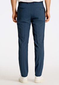 Skräddarsydda byxor i mörkblått tyg, slim fit, med två bakfickor med knappar och en slät textur. Bärs med vita sneakers.