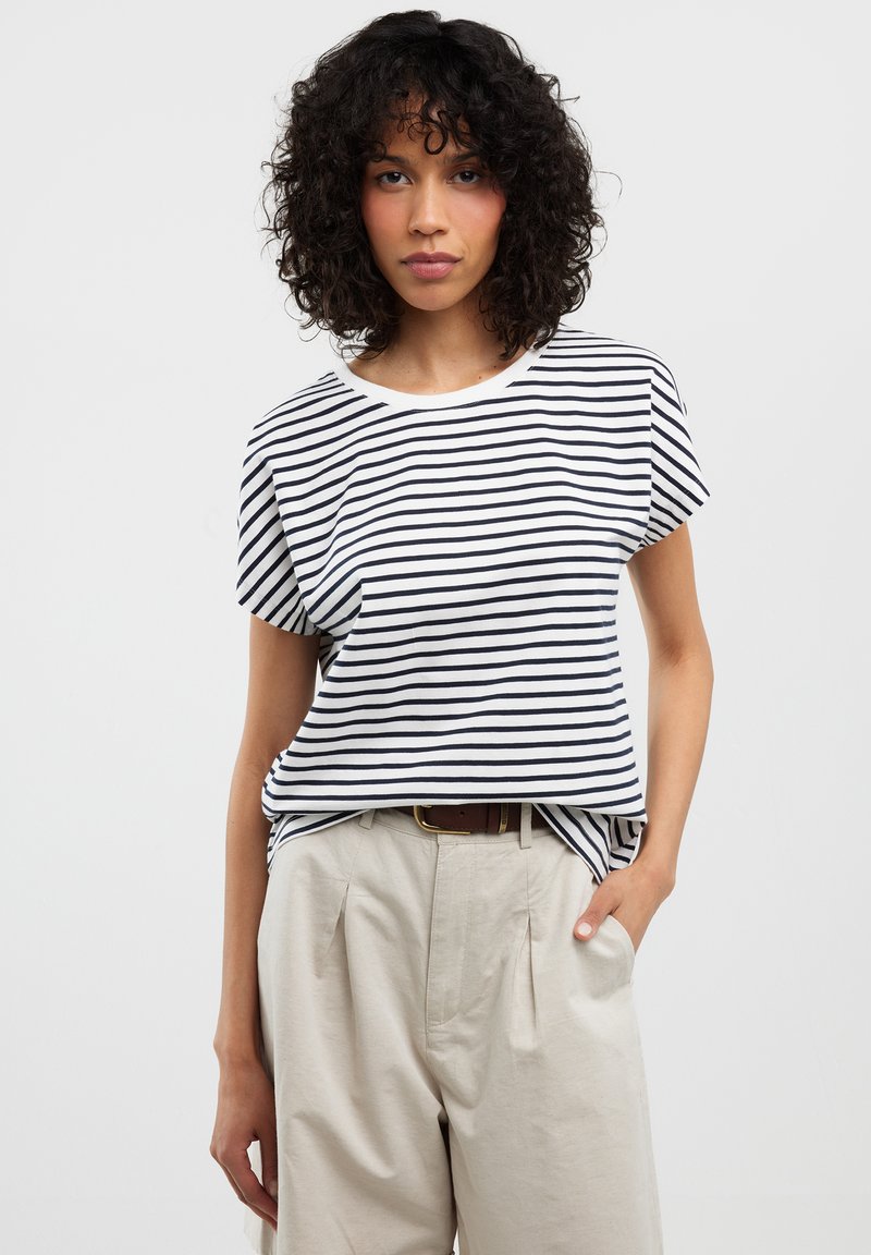 Trumpetakio trumpas rankovės baltas marškinėliai su tamsiai mėlynomis horizontaliomis juostelėmis. Minkšta medžiaga, apvalus iškirpimas, laisvas siluetas, derinami su aukšto liemens smėlio spalvos kelnėmis.