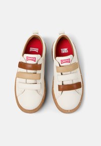 Baskets en cuir blanc avec des bandes Velcro marron et beige, semelle en caoutchouc beige, et accents rouges à l'intérieur ; le nom de la marque "Camper" est visible sur les étiquettes.