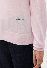 Ανοιχτό ροζ πουλόβερ από μαλακό ύφασμα, με ραμμένα μανίκια και στρίφωμα σε ριμπ, και με το πράσινο λογότυπο Calvin Klein ραμμένο στη χαμηλή πλευρά.