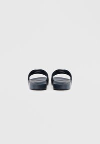 Nāvija zilas slidkalniņa sandaletes, izgatavotas no teksturēta, viegla materiāla ar atvērtu papēža dizainu un plakanu zolīti.