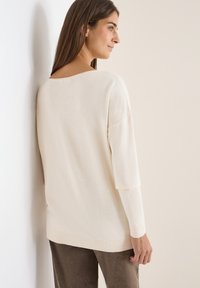 Cremefarbener Strickpullover mit lockerer Passform, der über Dreiviertelärmel und einen weiten Ausschnitt verfügt. Glatte Textur, minimalistische Details und gerippter Saum.