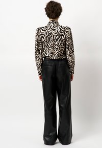 Patroonblouse in crème en zwart met lange mouwen; gecombineerd met hoogsluitende, wijde, gladde zwarte leren broeken.