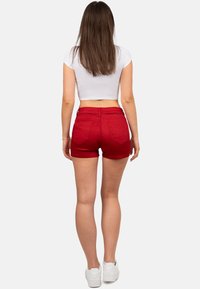 Pantaloni corti in denim rosso con vita alta, design a cinque tasche e orlo risvoltato, abbinati a una maglietta bianca cropped e scarpe da ginnastica bianche.