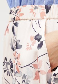 Kangas kukkakuosisella, jossa on vaaleanpunaisia, purppuran värisiä ja vihreitä yksityiskohtia. Sisältää poimutetun vyötärön ja sivutaskun, sekä pehmeän, kevyen tekstuurin.