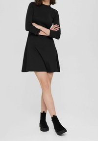 Svart långärmad klänning med en åtsittande midja och utställd kjol, tillverkad av slätt tyg. Kombinerad med svarta ankelstövlar med en tjock sula.