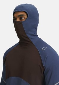 Base layer con cappuccio stile balaclava in blu e marrone scuro. Presenta una maschera per il viso perforata, texture liscia e cuciture a contrasto.