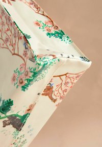 Boîte de rangement en tissu à motif floral, avec un fond crème, des accents verts et des illustrations d'animaux parmi des arbres et des fleurs.