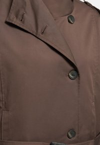 Palton maro cu guler larg, trei nasturi mari și întunecați și găici pentru nasturi, prezentând cusături detaliate și textura țesăturii.