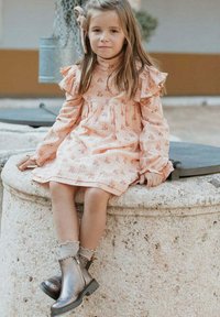 Vestido de manga larga de color rosa pastel con estampado floral y mangas con volantes; combinado con botas tobilleras metálicas plateadas y calcetines de canalé grises.