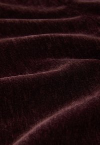 Bordeauxfarbener Stoff mit einer weichen, strukturierten Oberfläche, sanften Falten und subtilen Schattierungsvariationen, nah aufgenommen.