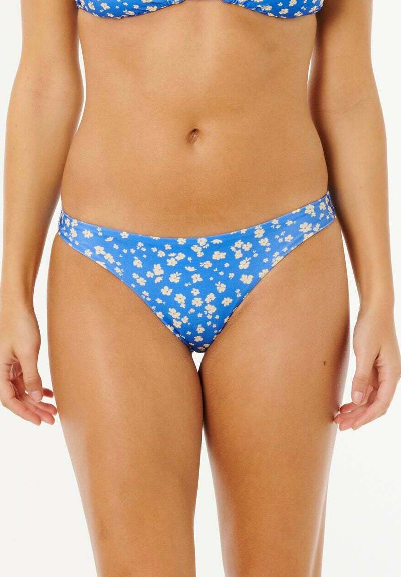 Frau trägt blaue Bikinihose mit weißem Blumenmuster, zeigt Taille, Hüften und obere Oberschenkel vor weißem Hintergrund.