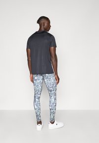 Sötét szürke rövid ujjú póló és világoskék terepmintás leggings, fehér sportcipővel párosítva, hátulról nézve.