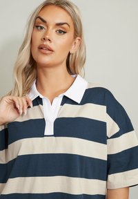 Randig polo med breda marinblå och gräddfärgade ränder, vit krage, korta ärmar och en avslappnad passform med mjuk textur.