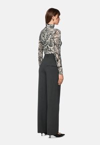 Long-sleeve, patterned top with a black-and-white cityscape design; paired with high-waisted, dark gray wide-leg trousers and black heels.