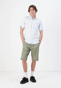 Light blue short-sleeve button-up shirt with a chest pocket, paired with olive green shorts. Black shoes and white socks complete the outfit.