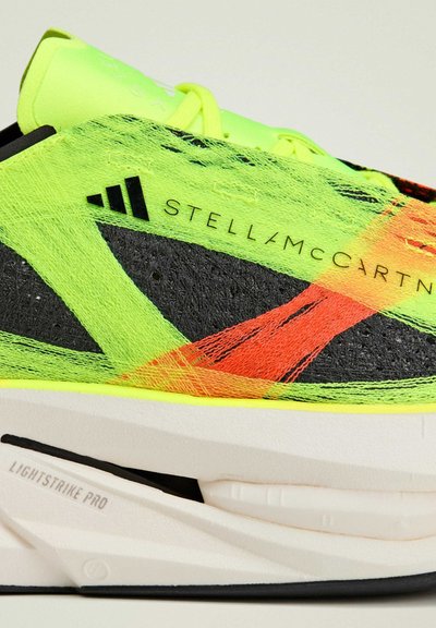 Chaussure de sport légère en jaune fluo et noir avec des accents orange vif, présentant un dessus texturé et une semelle blanche épaisse avec le logo "Lightstrike Pro".