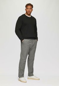 Zwarte sweatshirt met geribbelde boorden, gedragen over een witte t-shirt, gecombineerd met grijze gestreepte broek en witte sneakers. Staande pose, met handen in de zakken.
