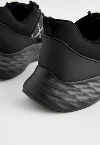 Black athletic shoes with a textured, molded foam sole. Features a smooth upper and elastic pull tabs for easy wear.