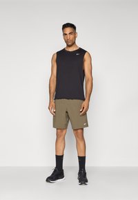 Débardeur noir sans manches, shorts verts olive, baskets noires et chaussettes noires. Design sportif simple avec des accents de logo de marque.