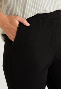 Pantalones ajustados negros con textura suave, que cuentan con bolsillos laterales y una cinturilla limpia, complementados por una blusa rayada y ligera.