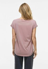 T-shirt rose clair avec des manches retroussées, texture lisse, ourlet arrondi et coupe décontractée, montré de l'arrière sur un modèle avec des cheveux ondulés.
