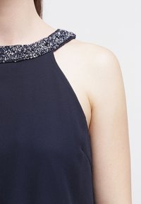 Marinblå ärmlös topp med en strukturerad pärlkrage med metalliska accenter, mjukt tyg och en avslappnad passform.