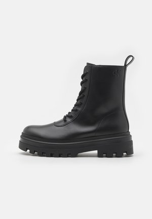 Zwart leren veterschoenen tot op de enkel met dikke profielzool, trek lus achterop en een gegraveerd "ck" logo vlak bij de bovenkant aan de buitenkant.