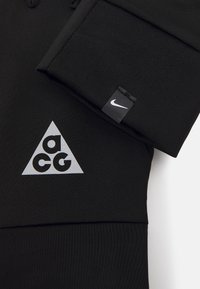 Nike black ACG hoodie featuring a triangular grey logo with "acg" text. Material is smooth, with subtle texture and stitching details.