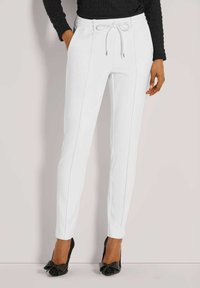 Witte, taps toelopende broek met een trekkoord in de tailleband, voorzien van twee zijzakken en contrasterende stiksels. G gedragen met zwarte hoge hakken.