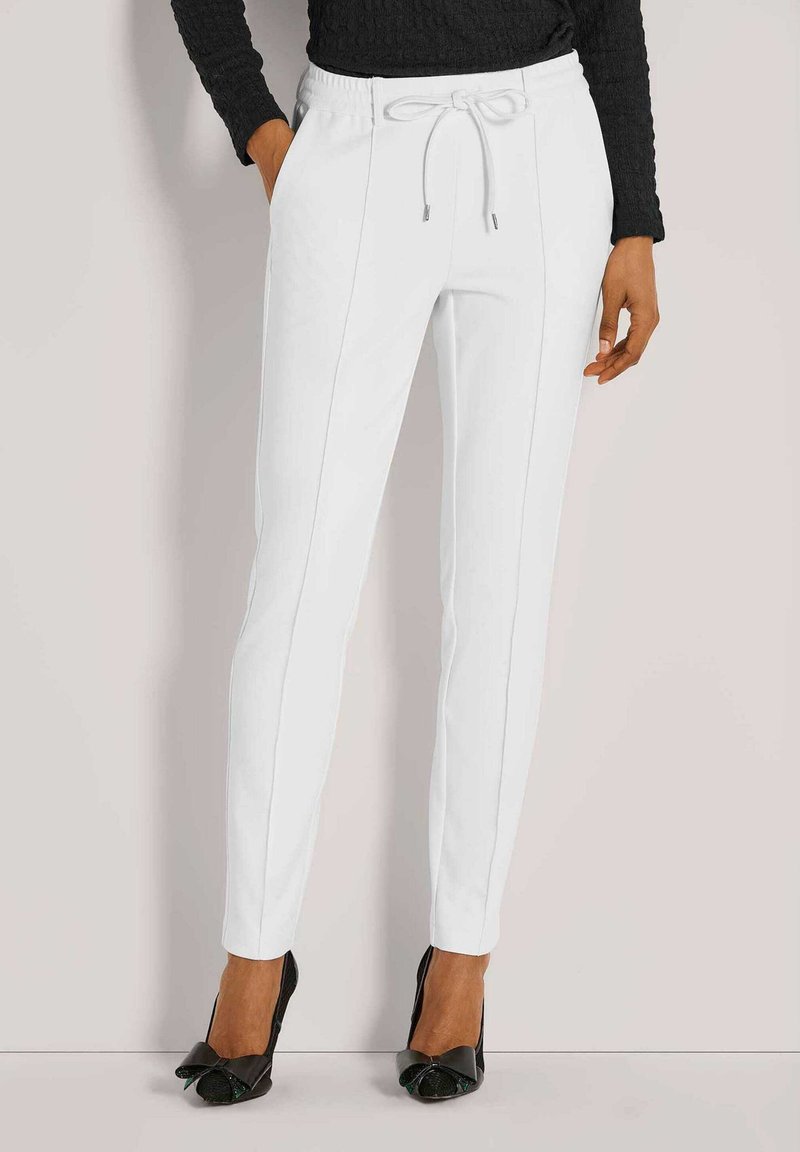 Witte, taps toelopende broek met een trekkoord in de tailleband, voorzien van twee zijzakken en contrasterende stiksels. G gedragen met zwarte hoge hakken.
