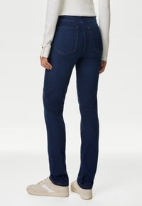 Mörkblå jeans med rak benkup, medelhög midja, två bakfickor och subtila sömnadsdetaljer, matchat med ljusa sneakers.
