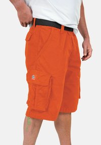 Pantaloni cargo arancioni con molte tasche, una cintura nera e un'etichetta prominente sulla tasca. Realizzati in tessuto resistente, design lungo fino al ginocchio.