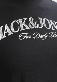 Tissu noir avec texte blanc "JACK & JONES" en grande police serif et "For Daily Use" en plus petite police cursive en dessous.