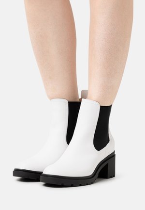 Bottines blanches en cuir avec des côtés en élastique noir, un talon épais et une semelle texturée pour une meilleure adhérence. Le design présente une finition lisse.