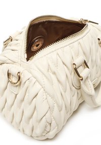 Borsa a tracolla in pelle bianca trapuntata con hardware dorato, cerniera aperta che mostra l'interno in tessuto marrone e un patch rotondo con logo all'interno.