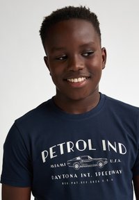 Námořnická modrá bavlněná tričko s potiskem "PETROL IND" a ilustrací auta. Krátké rukávy, kulatý výstřih, uvolněný střih.